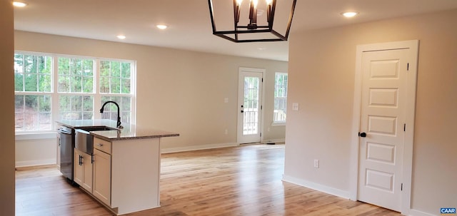 kitchen with light stone counters, white cabinetry, a center island with sink, light wood-type flooring, and dishwasher