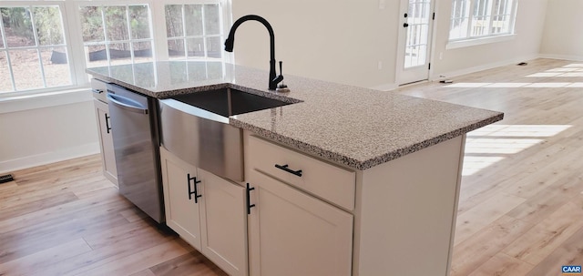 kitchen featuring sink, dishwasher, a kitchen island with sink, light stone countertops, and white cabinets