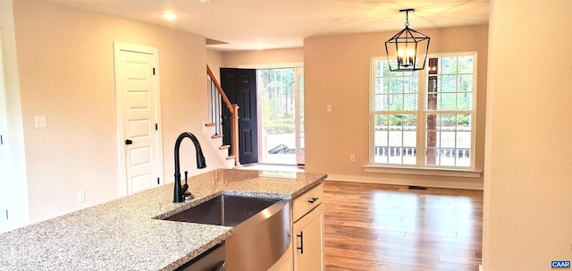 kitchen featuring a wealth of natural light, sink, hanging light fixtures, light stone countertops, and an inviting chandelier