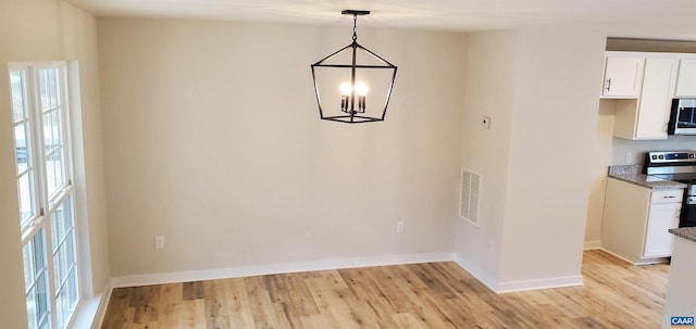 unfurnished dining area with a notable chandelier and light wood-type flooring