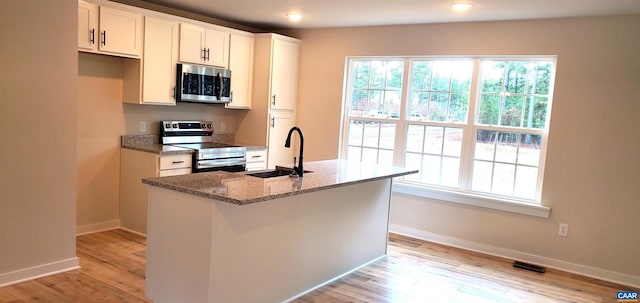 kitchen with sink, stone counters, white cabinetry, appliances with stainless steel finishes, and an island with sink