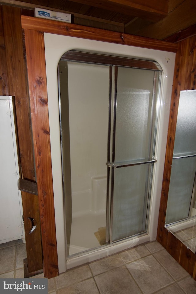 bathroom featuring tile patterned flooring, a shower with door, and wooden walls