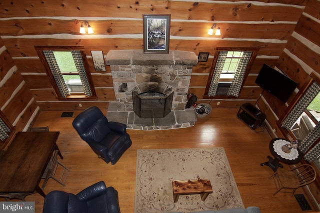 living room with hardwood / wood-style floors, wood walls, and a stone fireplace