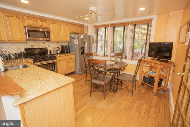 kitchen with backsplash, light hardwood / wood-style floors, sink, light stone countertops, and appliances with stainless steel finishes