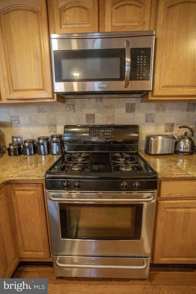 kitchen with stainless steel appliances, decorative backsplash, and light stone counters