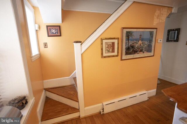 stairway with a baseboard heating unit and hardwood / wood-style flooring