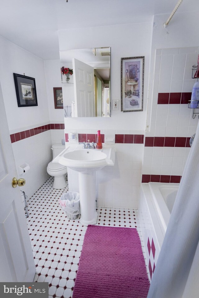 bathroom with tiled bath, tile walls, toilet, and tile patterned flooring