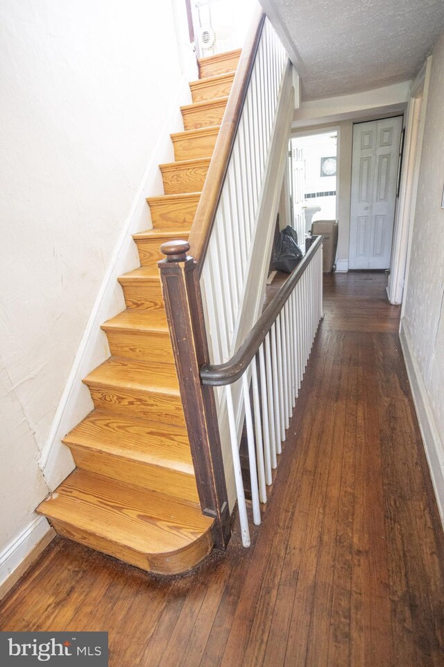 stairway with a textured ceiling and hardwood / wood-style floors