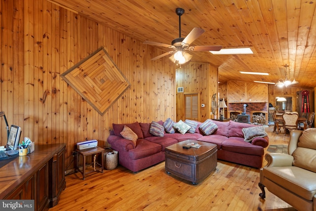 living room with wood ceiling, ceiling fan, a skylight, light hardwood / wood-style floors, and wood walls