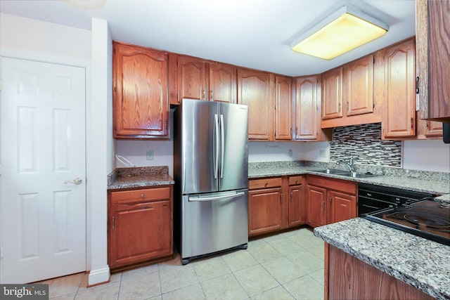 kitchen featuring sink, light stone counters, stainless steel refrigerator, and decorative backsplash