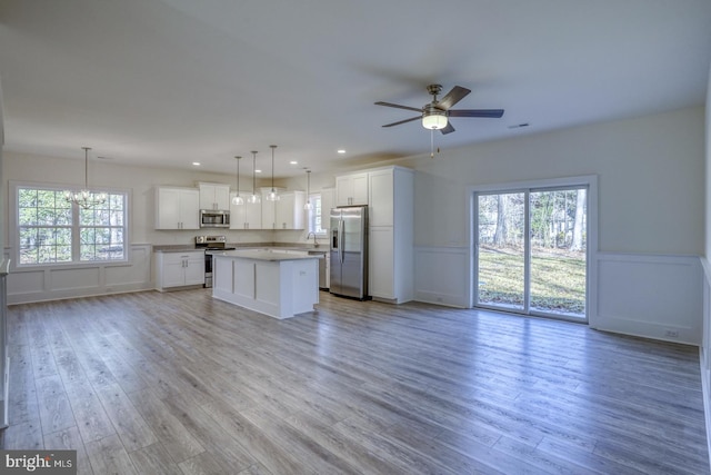 kitchen with white cabinetry, a center island, stainless steel appliances, pendant lighting, and ceiling fan with notable chandelier