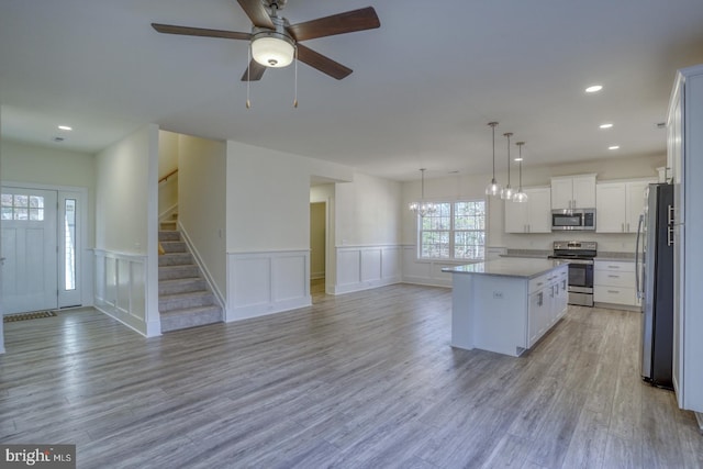 kitchen featuring appliances with stainless steel finishes, light hardwood / wood-style flooring, white cabinets, a kitchen island, and hanging light fixtures