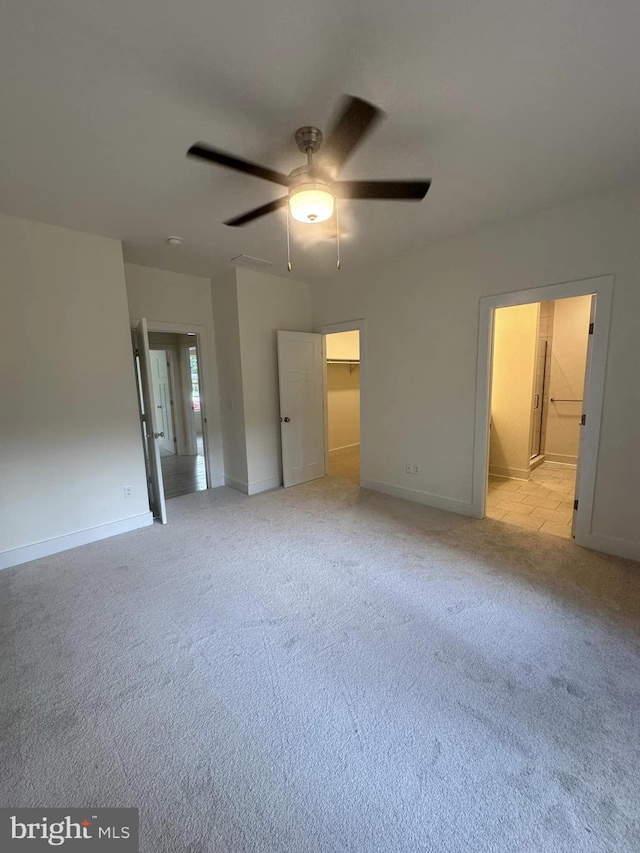 unfurnished bedroom with ceiling fan, a spacious closet, connected bathroom, light colored carpet, and a closet