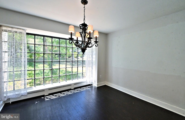 unfurnished dining area featuring dark wood-type flooring, a baseboard heating unit, and a notable chandelier