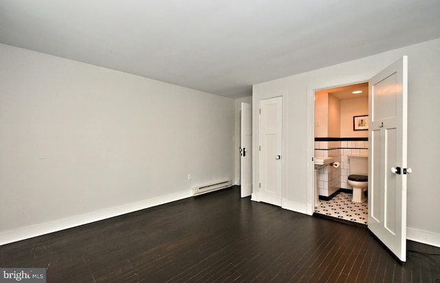 unfurnished bedroom featuring a baseboard heating unit, dark hardwood / wood-style flooring, and connected bathroom