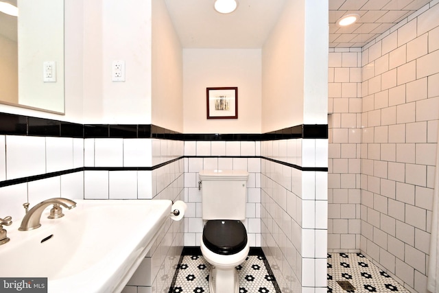 bathroom with toilet, sink, tile walls, and tile patterned floors