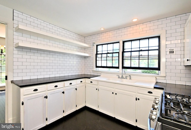 kitchen featuring stainless steel range, white cabinetry, backsplash, and sink