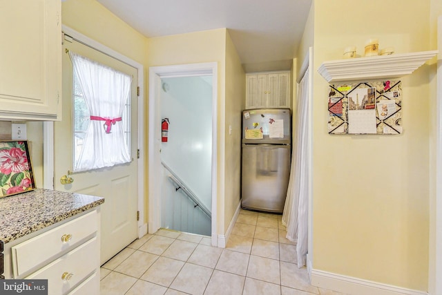 kitchen featuring light stone countertops, a wealth of natural light, stainless steel fridge, and light tile patterned flooring