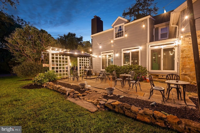 back house at dusk featuring a lawn and a patio