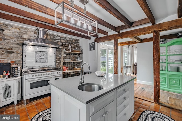 kitchen with wall chimney exhaust hood, sink, white cabinetry, a center island with sink, and double oven range