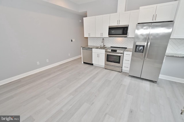 kitchen with light stone countertops, white cabinetry, appliances with stainless steel finishes, and light hardwood / wood-style flooring