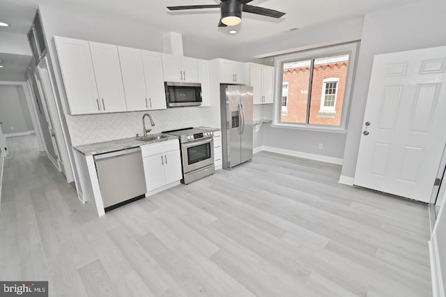 kitchen with sink, light hardwood / wood-style flooring, decorative backsplash, appliances with stainless steel finishes, and white cabinetry