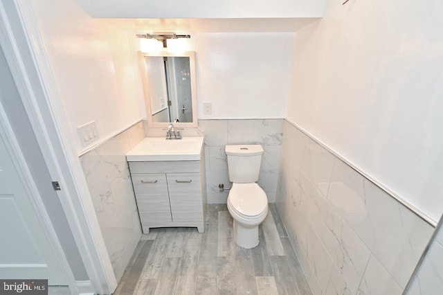 bathroom with hardwood / wood-style flooring, vanity, tile walls, and toilet