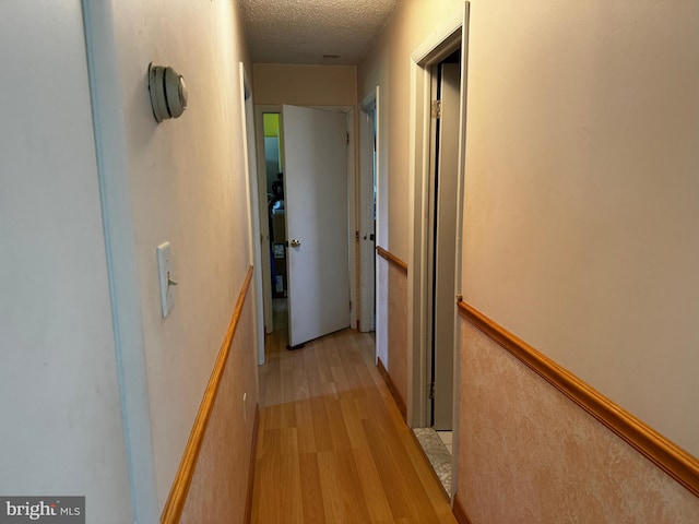 corridor with a textured ceiling and light hardwood / wood-style floors