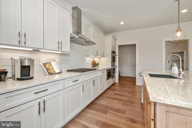 kitchen featuring wall chimney range hood, light wood-type flooring, sink, light stone countertops, and backsplash