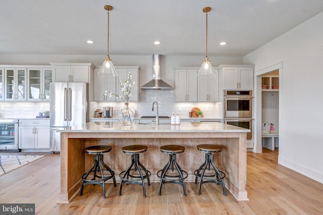 kitchen with appliances with stainless steel finishes, tasteful backsplash, light wood-type flooring, and wall chimney exhaust hood