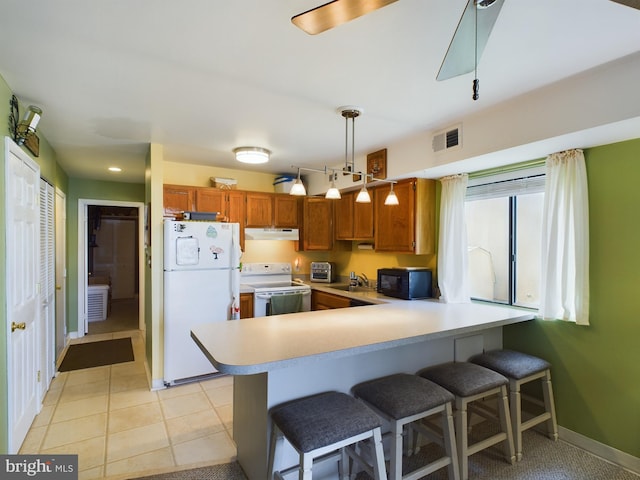 kitchen featuring under cabinet range hood, light countertops, a peninsula, brown cabinetry, and white appliances