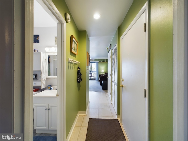 hallway featuring light tile patterned flooring, baseboards, and a sink