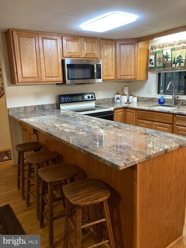 kitchen featuring a kitchen bar, sink, stone countertops, electric range, and kitchen peninsula