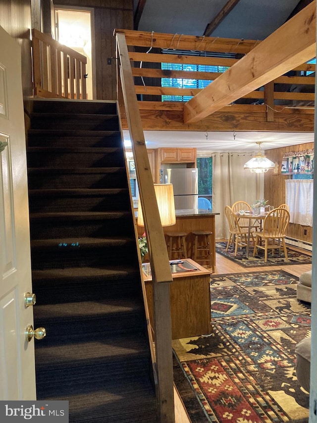 stairway featuring a baseboard heating unit and wood walls