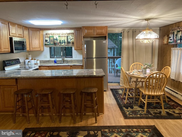 kitchen with appliances with stainless steel finishes, sink, a breakfast bar area, dark stone counters, and light hardwood / wood-style flooring