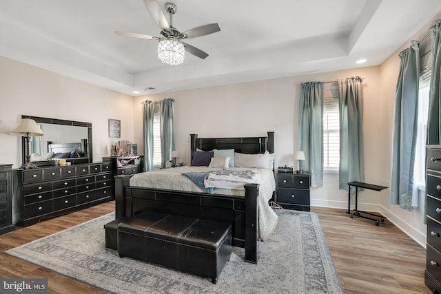 bedroom featuring light hardwood / wood-style floors, ceiling fan, and a raised ceiling