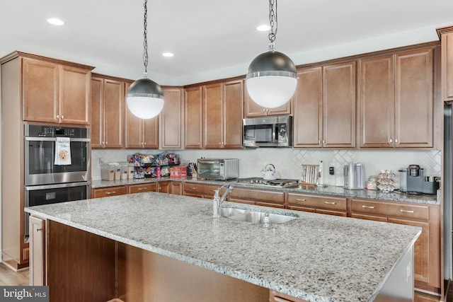 kitchen featuring decorative backsplash, appliances with stainless steel finishes, pendant lighting, and an island with sink