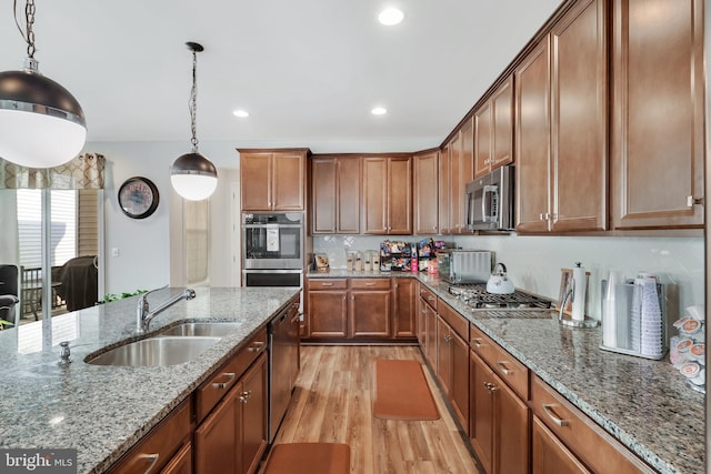 kitchen with light wood-type flooring, stainless steel appliances, hanging light fixtures, stone countertops, and sink