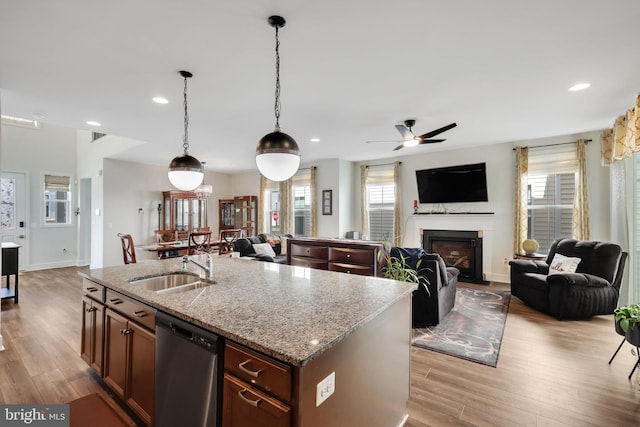 kitchen with stainless steel dishwasher, light wood-type flooring, light stone countertops, and an island with sink