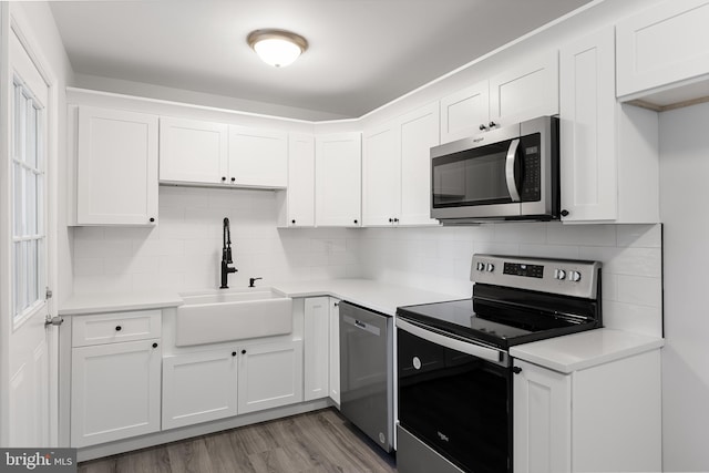 kitchen with appliances with stainless steel finishes, backsplash, sink, light hardwood / wood-style flooring, and white cabinets