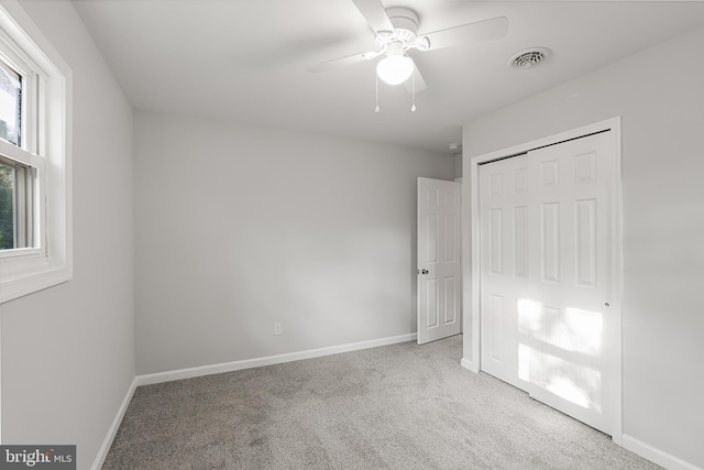 unfurnished bedroom featuring a closet, light colored carpet, multiple windows, and ceiling fan