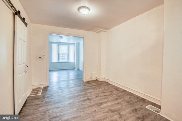 unfurnished room with a barn door and wood-type flooring