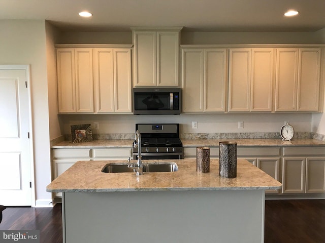 kitchen featuring stainless steel appliances, sink, light stone counters, an island with sink, and dark wood-type flooring