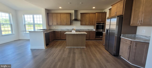 kitchen with stainless steel appliances, a center island, wall chimney exhaust hood, light stone countertops, and dark wood-type flooring