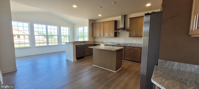 kitchen with appliances with stainless steel finishes, a center island, vaulted ceiling, wall chimney range hood, and dark wood-type flooring