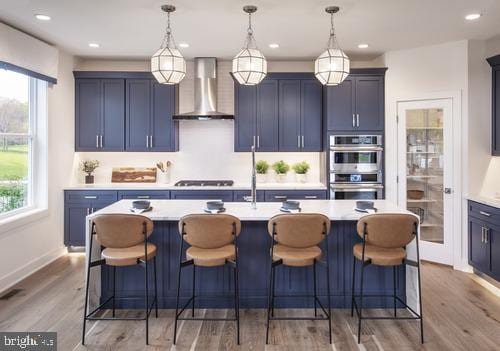 kitchen featuring wall chimney range hood, a kitchen island with sink, hanging light fixtures, and gas cooktop