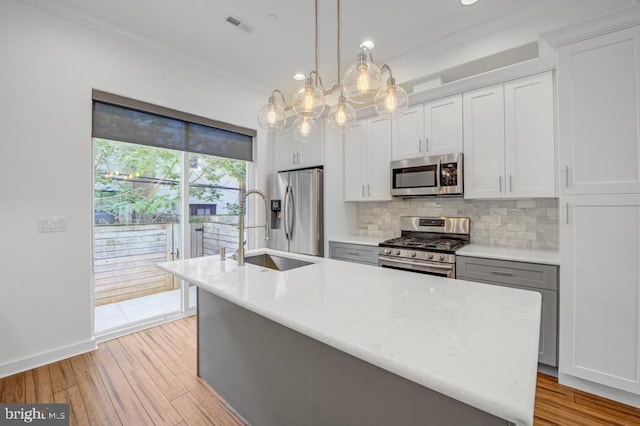 kitchen featuring backsplash, a center island with sink, crown molding, appliances with stainless steel finishes, and decorative light fixtures