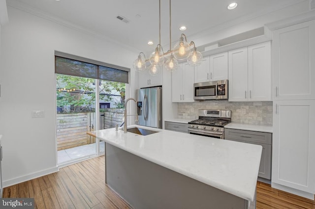 kitchen featuring tasteful backsplash, stainless steel appliances, crown molding, decorative light fixtures, and an island with sink