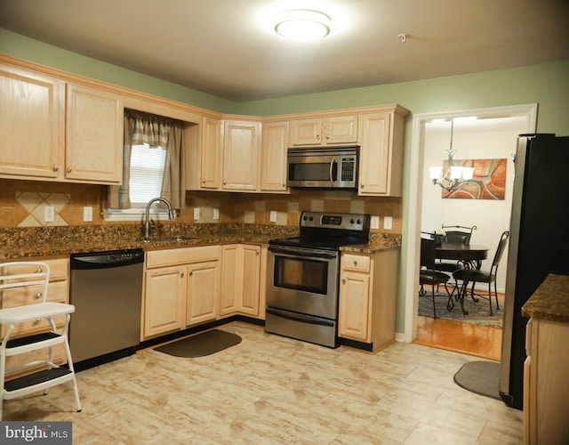 kitchen with dark stone countertops, pendant lighting, sink, an inviting chandelier, and appliances with stainless steel finishes