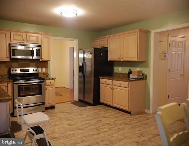 kitchen with light brown cabinetry, dark stone countertops, and stainless steel appliances